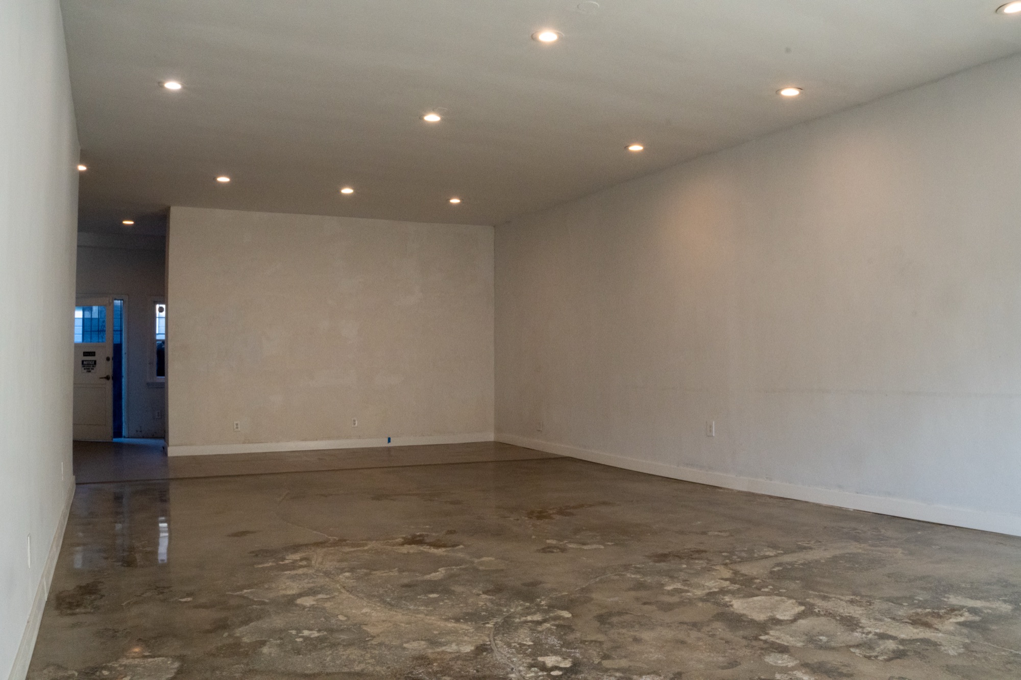 The vacant interior of 3815 W. Sunset Blvd. looking toward the rear: white walls, a full-height dividing partition, polished concrete floor, and recessed ceiling lighting.